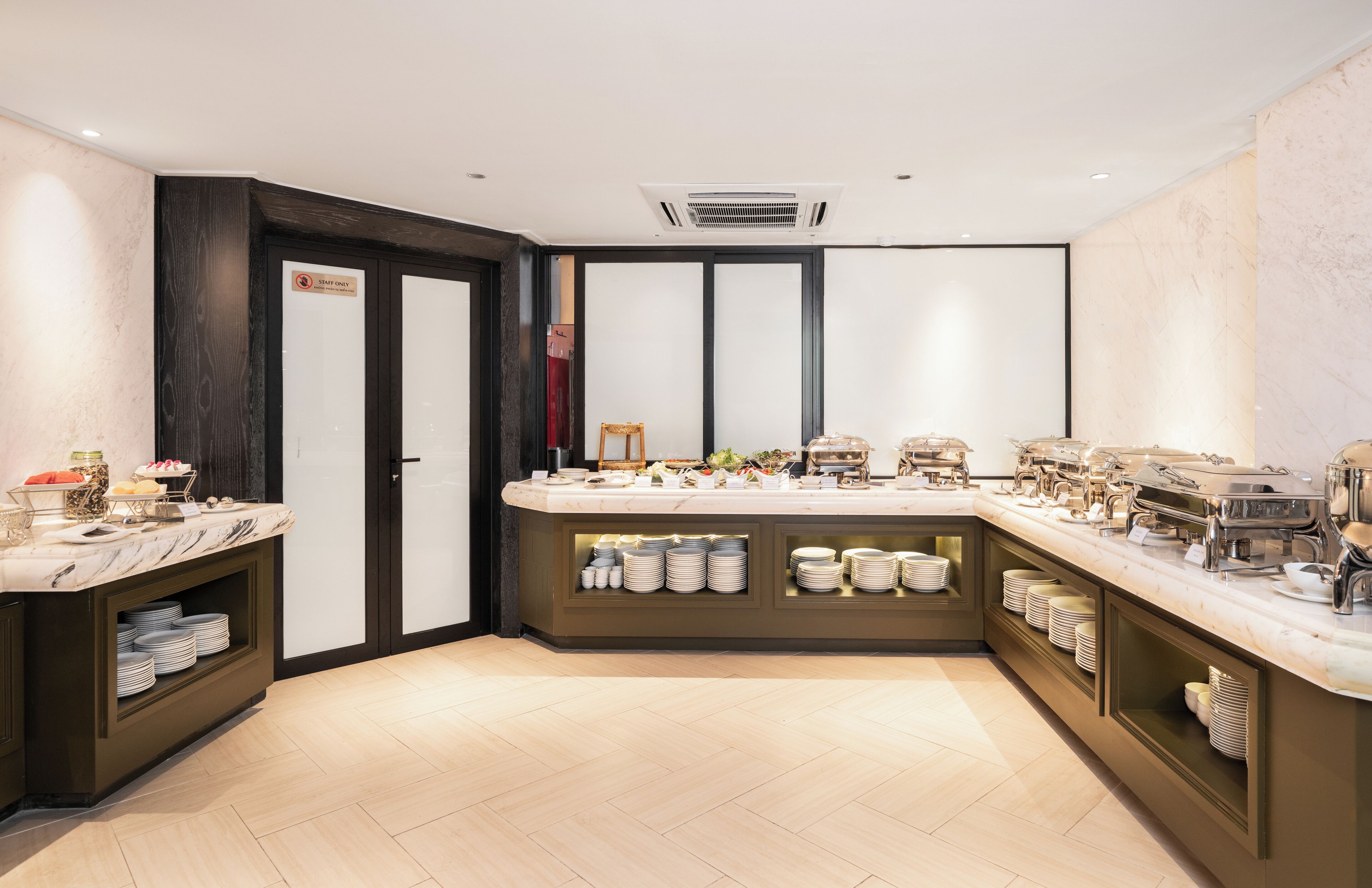 A modern buffet setup with multiple serving stations, a marble countertop, and neatly arranged plates and bowls.