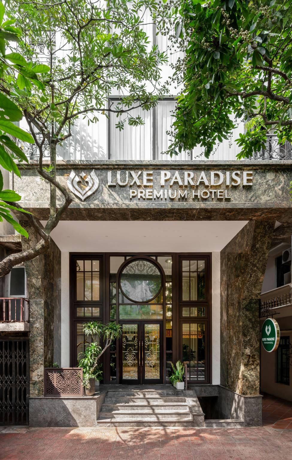 La entrada al hotel Luxe Paradise Premium, con fachada de piedra, puertas de cristal amplias y un ventanal circular central.