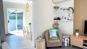 A modern living room with a sofa, a coffee table, a TV stand, and a bookshelf. There is a sliding glass door leading to a patio area with outdoor furniture. - 🔆GREENVIEW🔆BFast,WiFi,Fetch🔆Walk2Pizza,Liquor (Bell Post Hill)