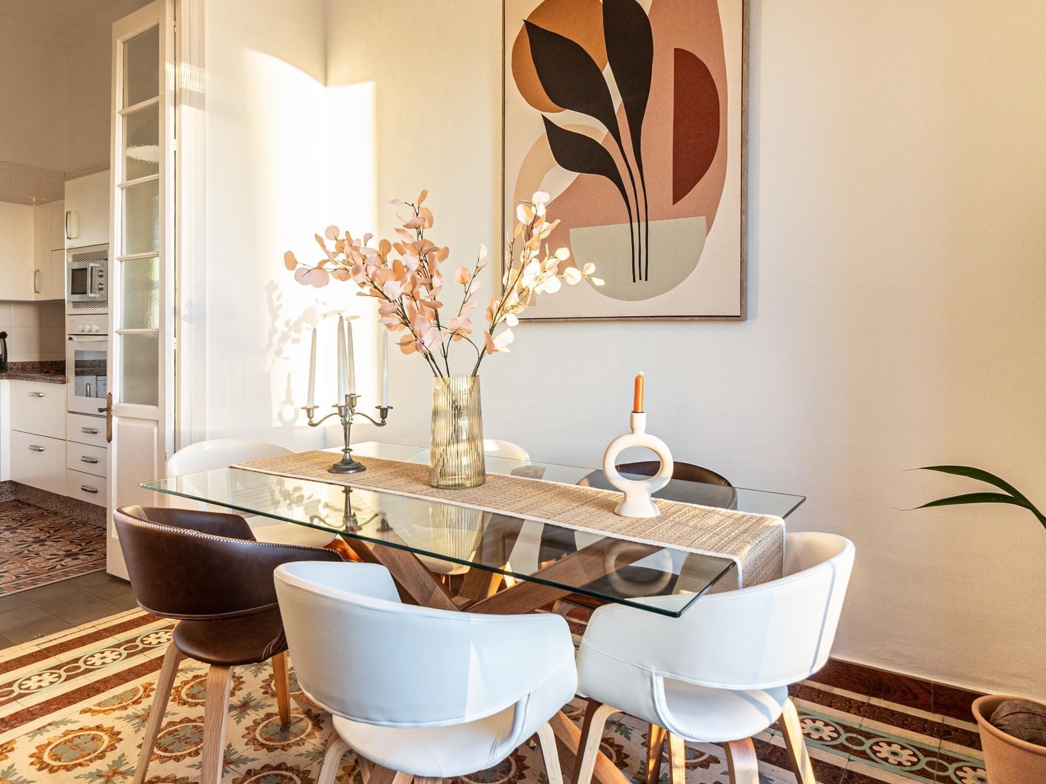 Un espace repas moderne avec une table en verre, des chaises blanches, un vase rempli de fleurs et un grand tableau abstrait accroché au mur.
