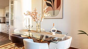 Un espace repas moderne avec une table en verre, des chaises blanches, un vase rempli de fleurs et un grand tableau abstrait accroché au mur.