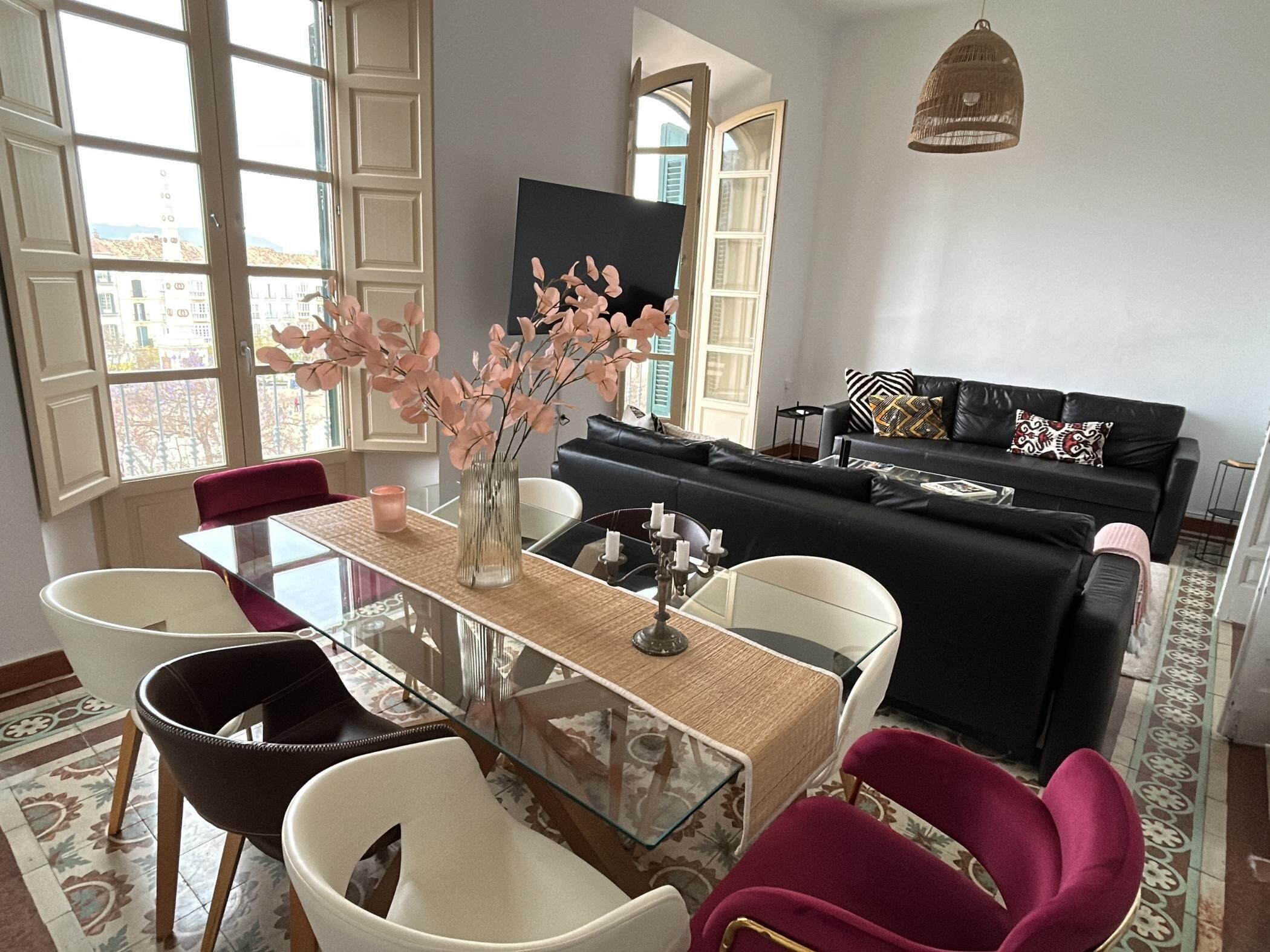 Un salon moderne avec une table à manger en verre, un canapé noir et blanc et un vase rempli de fleurs roses.