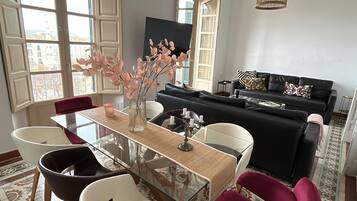 Un salon moderne avec une table à manger en verre, un canapé noir et blanc et un vase rempli de fleurs roses.