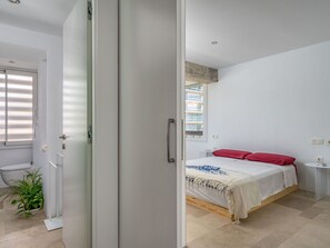 Ein Schlafzimmer mit Bett, Nachttisch, Fenster mit Jalousien und einer Zimmerpflanze.