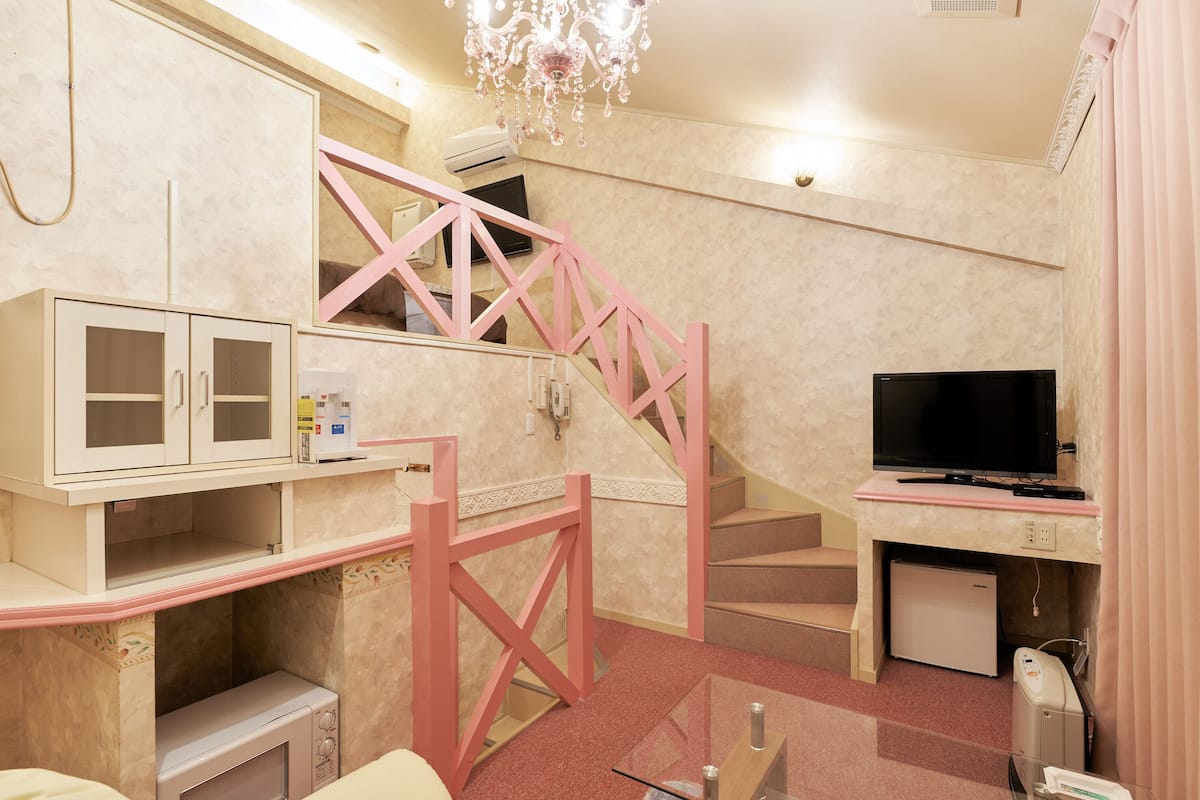 Hotellihuone, jossa on vaaleanpunainen portaikko, taulutelevisio, minibaari ja pieni jääkaappi.