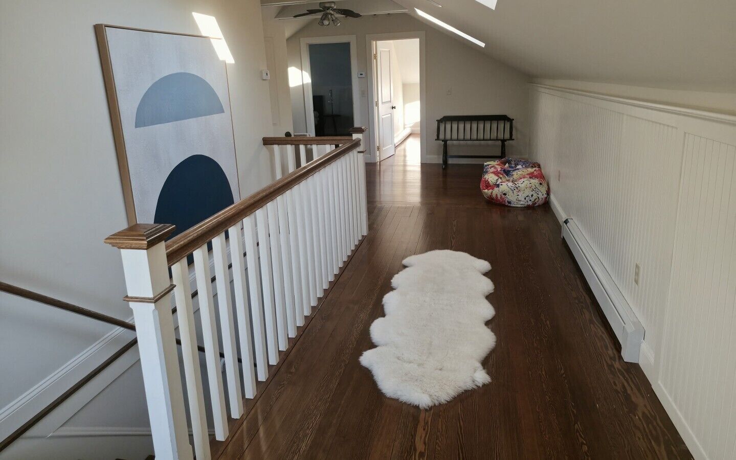 A hallway with a wooden floor, white railing, and a white shag rug.