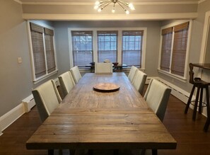 A dining room with a long wooden table, six chairs, a central round table, and a chandelier. - Middletown Bungalow w/Hot Tub and Private Yard - RIBryan Properties (Middletown)