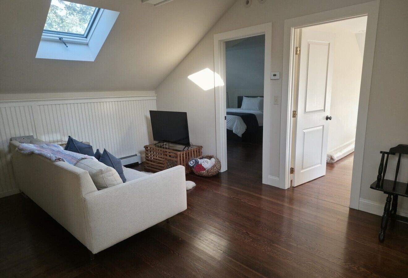Une pièce avec un canapé blanc, un téléviseur, un plancher en bois et une lucarne.
