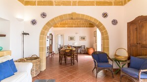 Àmplia zona d'estar amb una taula de menjador, cadires i un sofà. Un arc d'entrada condueix a una altra habitació.