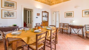 Una sala menjador amb una taula preparada per a quatre, envoltada de cadires de fusta. Hi ha quadres als murs, un moble de bany i una porta que dona a una altra habitaci ó.