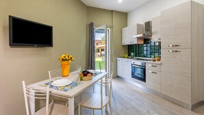 Eine moderne Küche mit weißen Schränken, einem an der Wand montierten Flachbildfernseher und einer Essecke mit Tisch für zwei Personen.