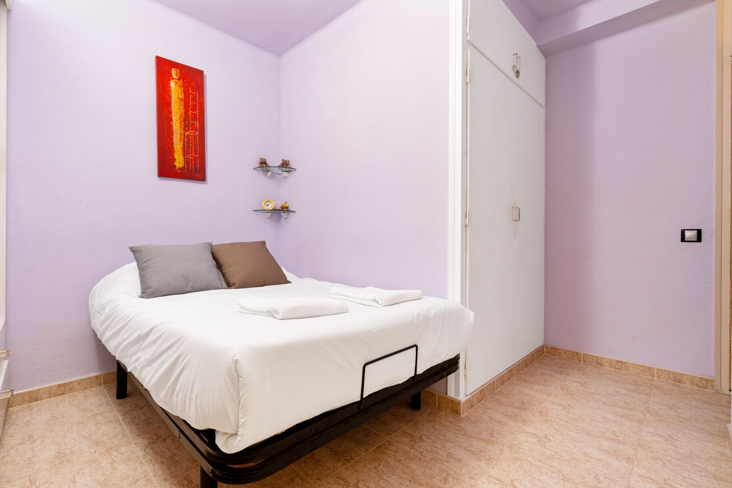 Un dormitorio con cama, un cuadro abstracto rojo, dos estanterías pequeñas y un armario.