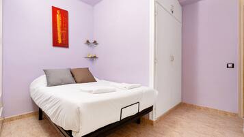 Un dormitorio con cama, un cuadro abstracto rojo, dos estanterías pequeñas y un armario.