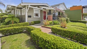 A two-story house with a red door, white porch, and a well-maintained garden with hedges and plants. - 1 Mile to the Beach, Games, Remodeled 3BD Home, Fire Pit, Patio (Long Beach)