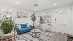A modern living room with a blue sofa, a round coffee table, and a large plant. - 1 Mile to the Beach, Games, Remodeled 3BD Home, Fire Pit, Patio (Long Beach)