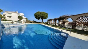 A swimming pool with clear blue water, surrounded by a white fence, a large tree, and a building with arches. - 17 - sea view Apt. in Calahonda (Mijas Costa)