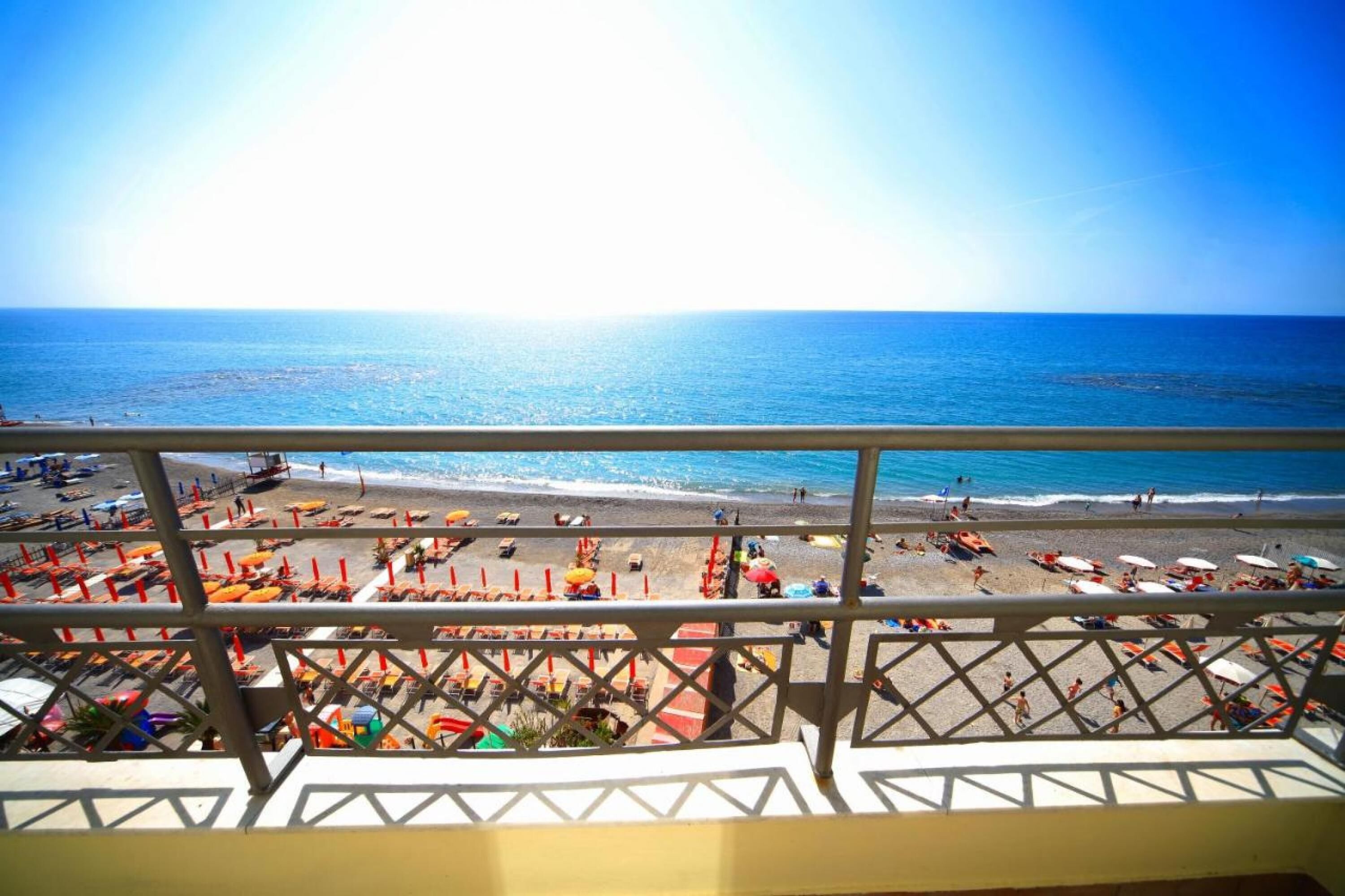 A beach view from a balcony with a railing, beach umbrellas, and people on the sand.