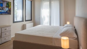 Hotellihuone, jossa on sänky, yöpöytälamppu, lipasto ja seinälle asennettu televisio.