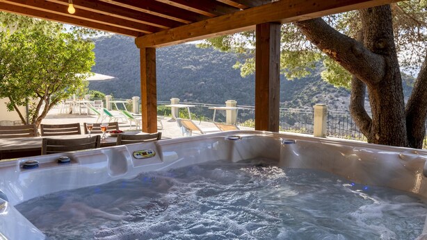 Een bubbelbad met een houten pergola erboven, omringd door lounge stoelen en tafels, met uitzicht op een bergachtig landschap.