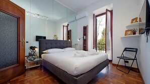 A modern bedroom with a large bed, a flat-screen TV, and a small table with a lamp. - 4bnb - Donatello Apartment (Rome)