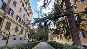 A narrow pathway flanked by buildings with multiple windows and a tree in the center. - 4bnb - Donatello Apartment (Rome)