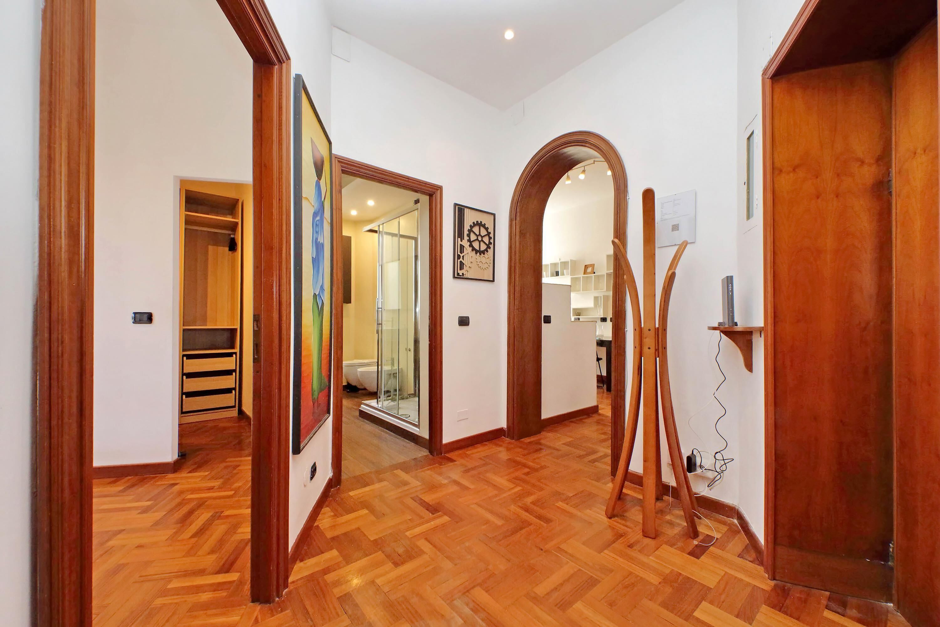 A hallway with wooden flooring, a wooden door, and a glass door leading to a bathroom.