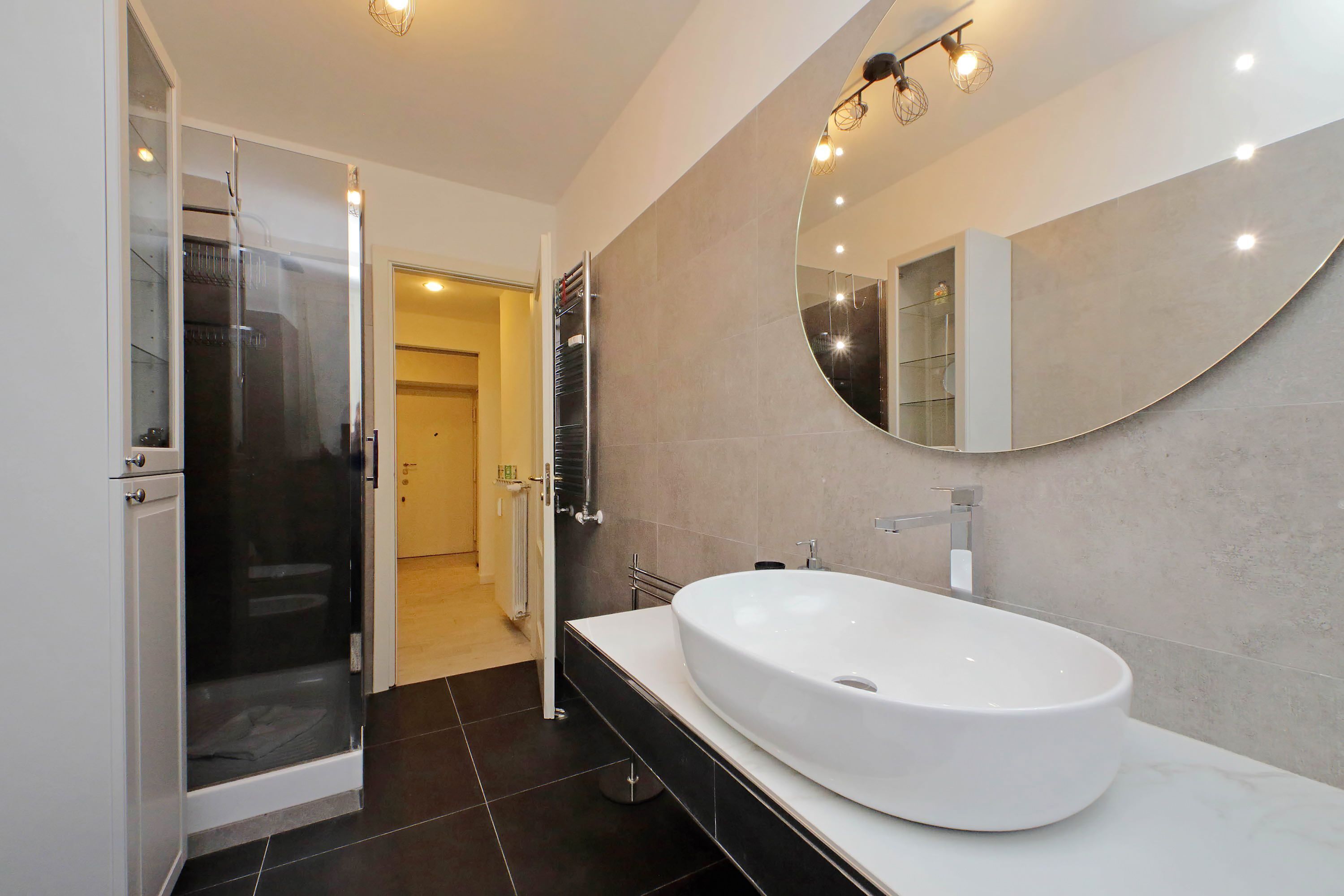 A modern bathroom with a large oval sink, a walk-in shower, and a large mirror.