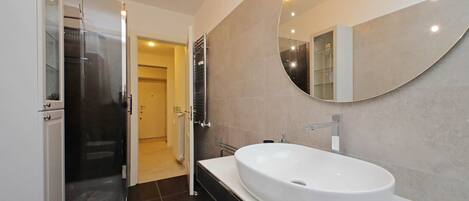 A modern bathroom with a large oval sink, a walk-in shower, and a large mirror.