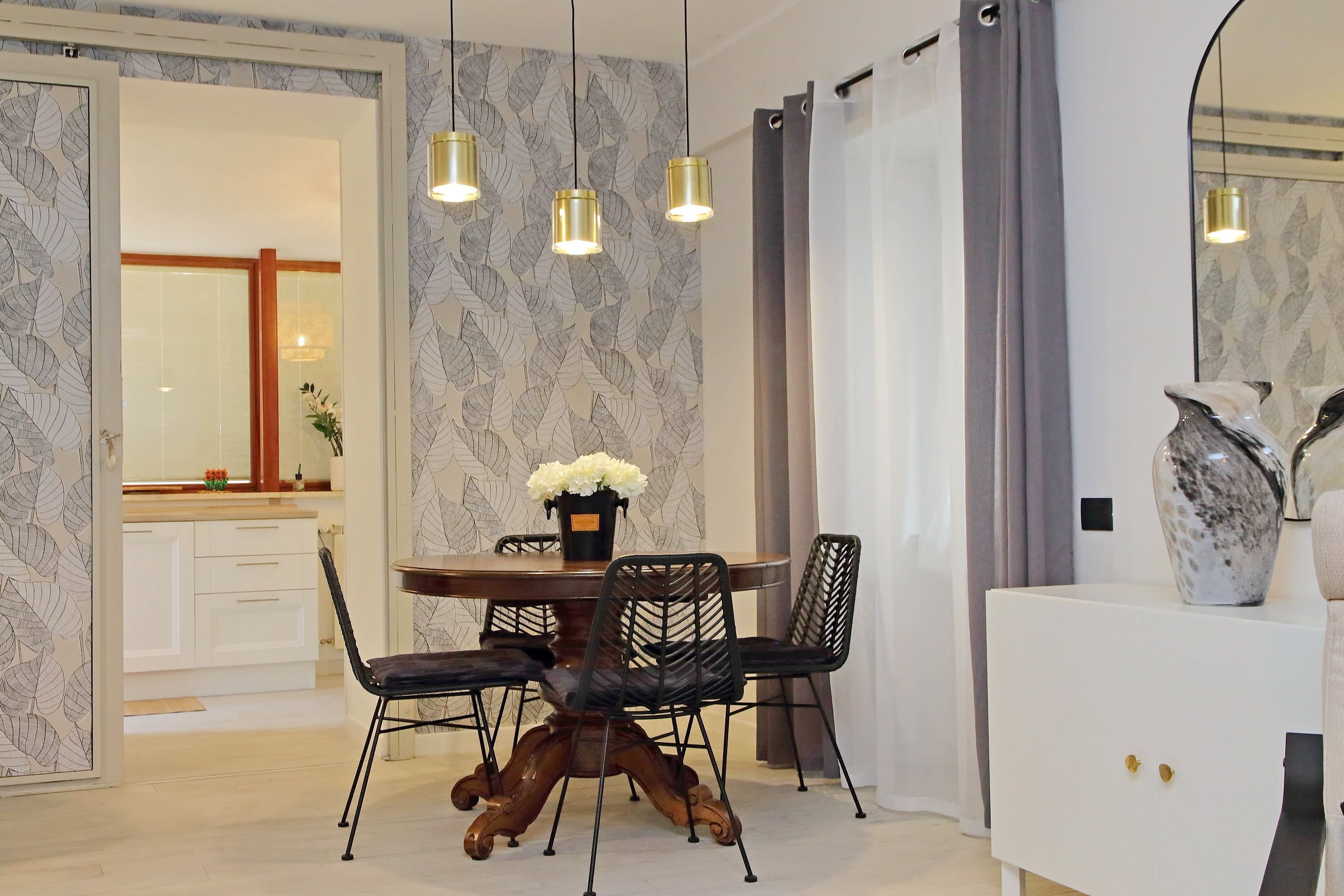 A dining area with a round table, black chairs, and a vase of flowers. There are three pendant lights above the table.