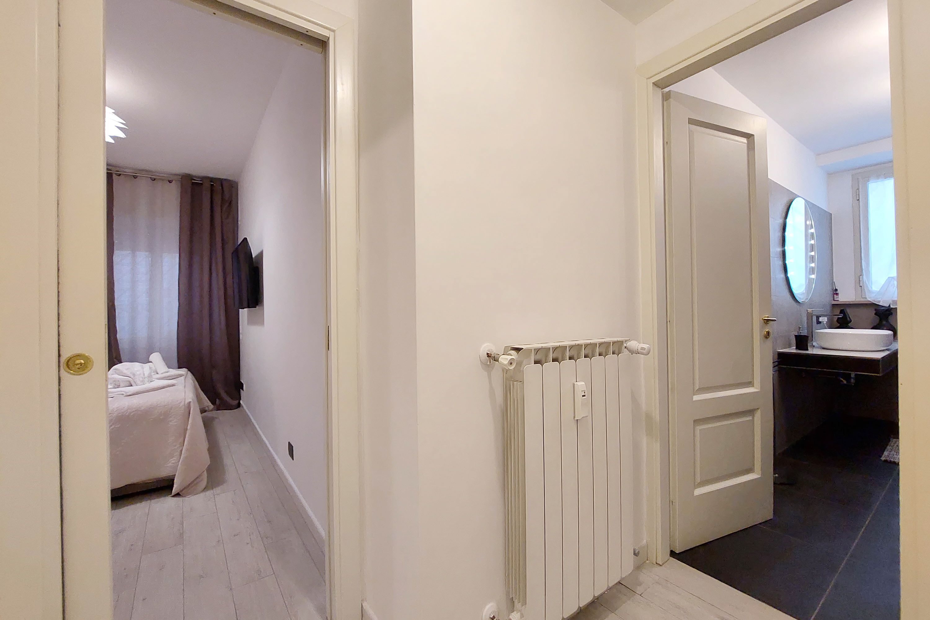 A hotel room with a bed, a radiator, and a bathroom with a sink and mirror.