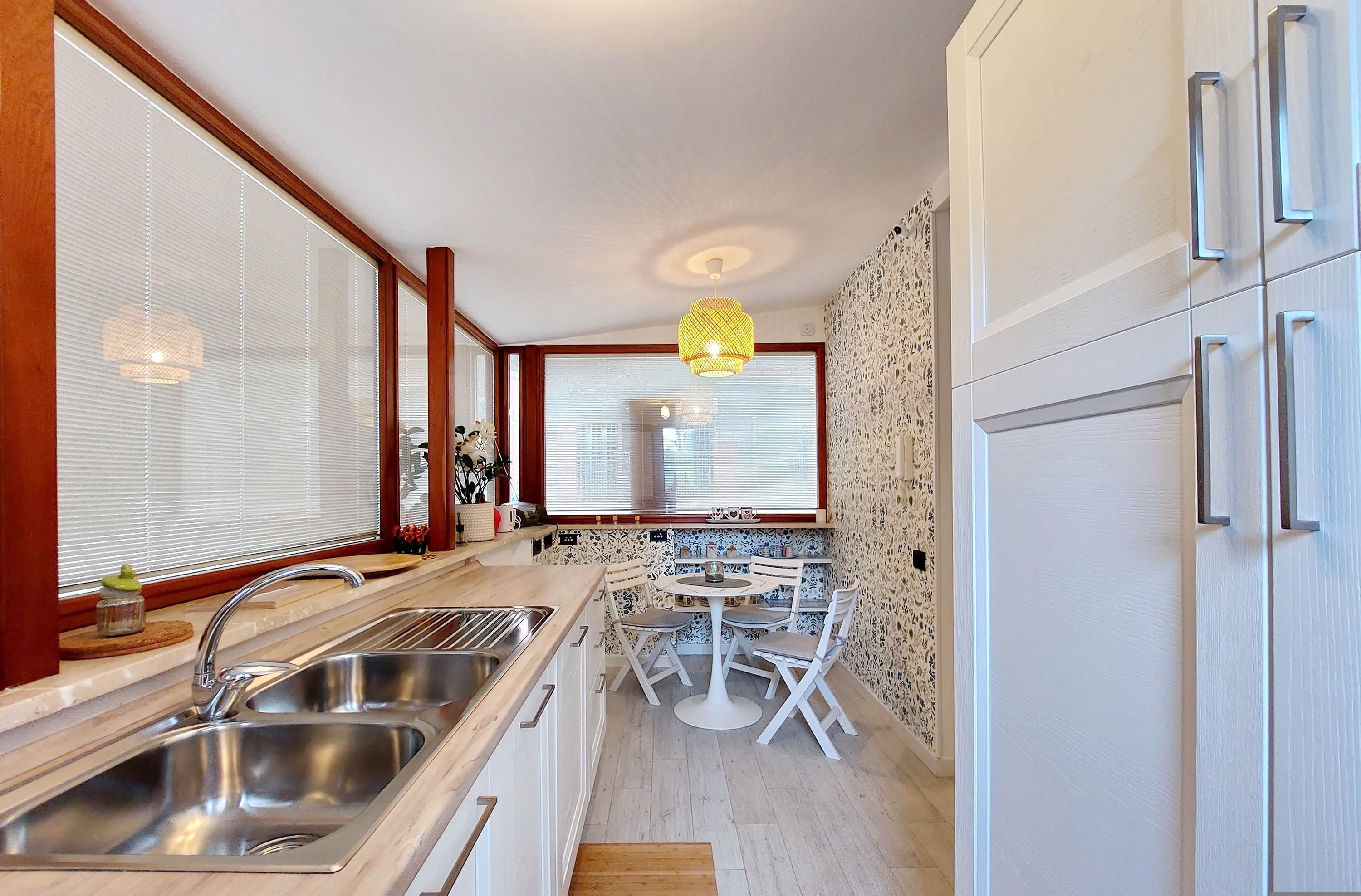 A modern kitchen with a double sink, white cabinetry, a round dining table with chairs, and a window with blinds.