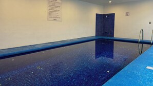 Una piscina interior con agua cristalina, un borde de azulejos azules y un cartel con normas.
