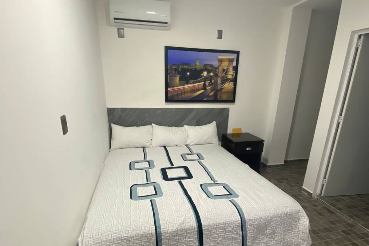 Una habitación de hotel con una cama, una mesita de noche, un cuadro en la pared y una puerta.