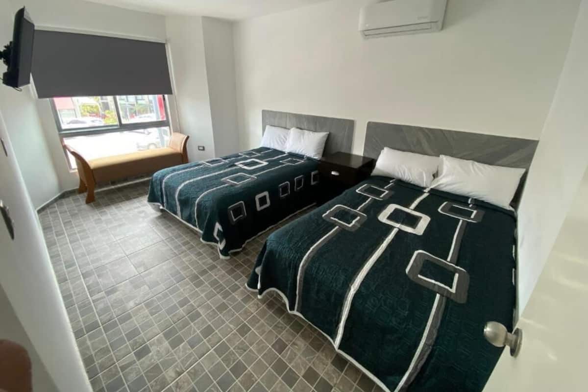 Habitación de hotel con dos camas, televisión, aire acondicionado y ventana con vista a la calle.