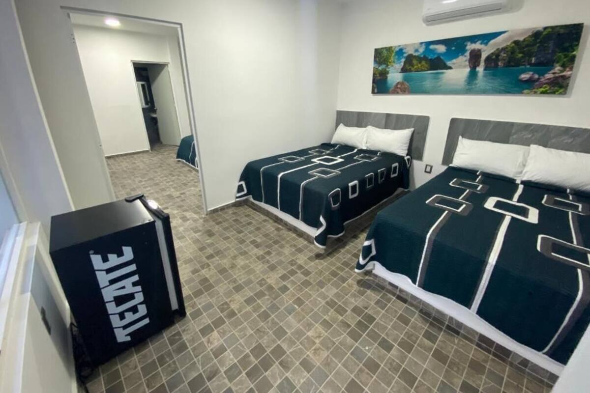 Habitación de hotel con dos camas, un ventanal grande y un cuadro de una escena costera.