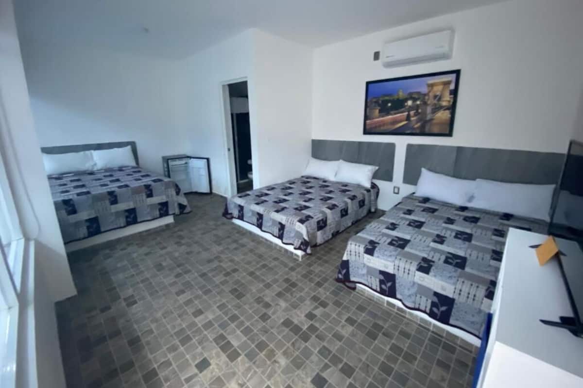 Habitación de hotel con dos camas, un escritorio y una silla. Hay un cuadro en la pared y una ventana con vista a edificios.
