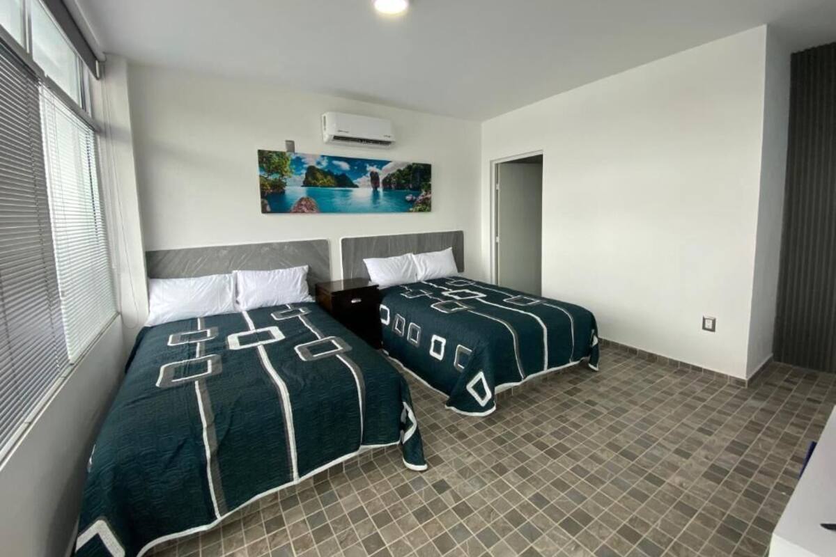 Habitación de hotel con dos camas, un cuadro en la pared y suelo de baldosas.