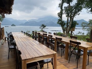 Eine Holzterrasse mit Tischen und Stühlen mit Blick auf einen See und Berge im Hintergrund.