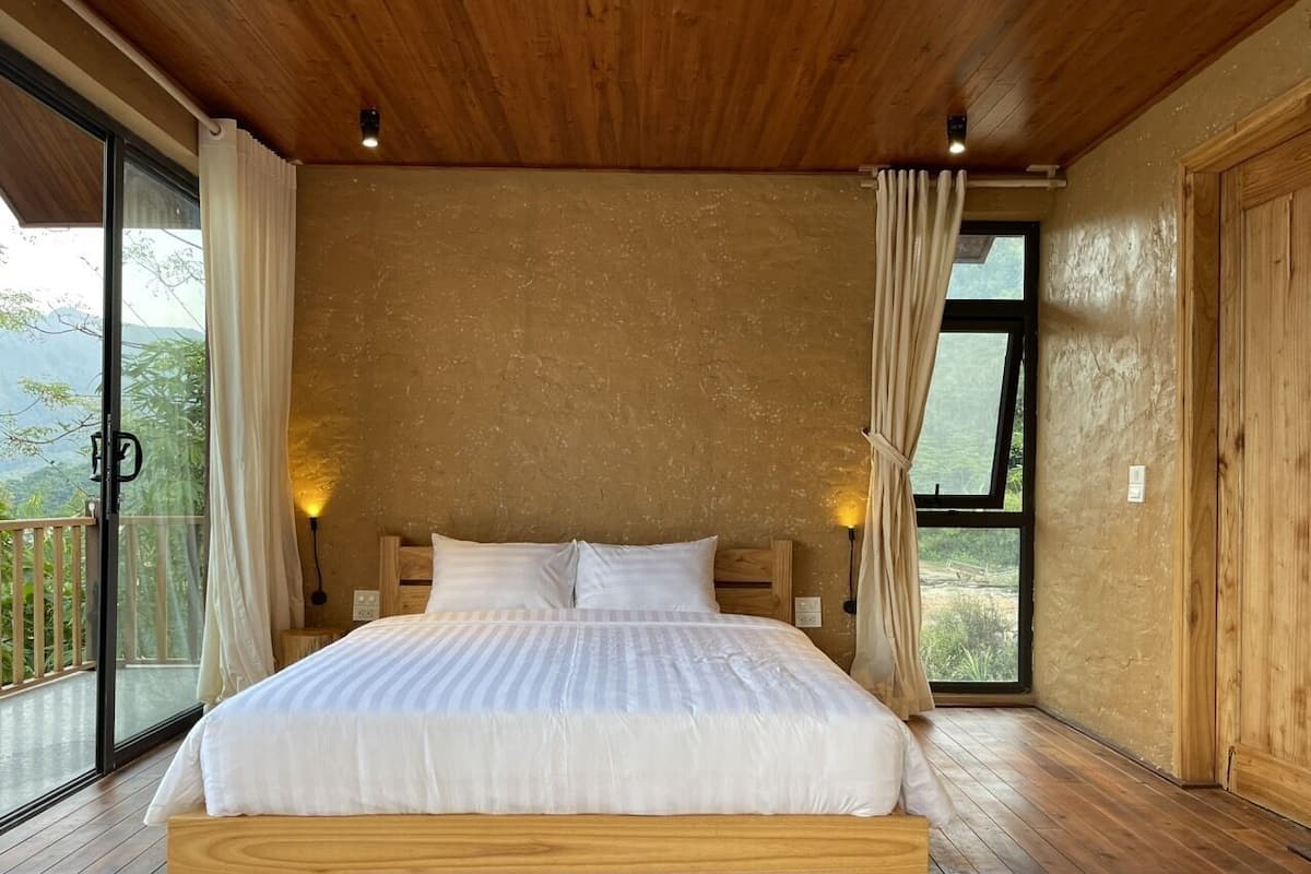 Un dormitorio amplio con una cama grande, suelo de madera y un balcón con vistas al exterior.