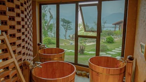 A room with large wooden barrels, a wooden ladder, and a view of a garden through large windows. - Mơ Village (Da Bac)