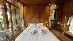 A large bed with a heart-shaped towel arrangement, wooden walls, and a view of greenery through large windows. - Mơ Village (Da Bac)