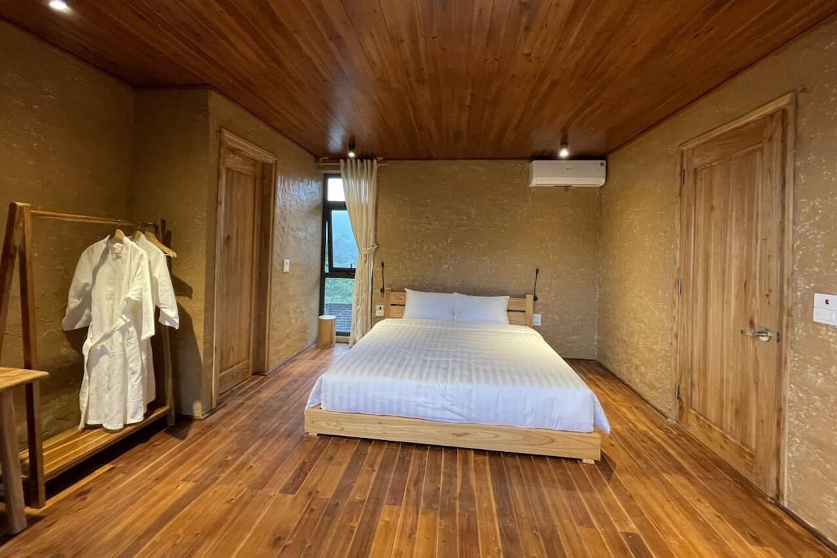 Un dormitorio con piso de madera, una cama con ropa blanca, un armario de madera y un espejo.