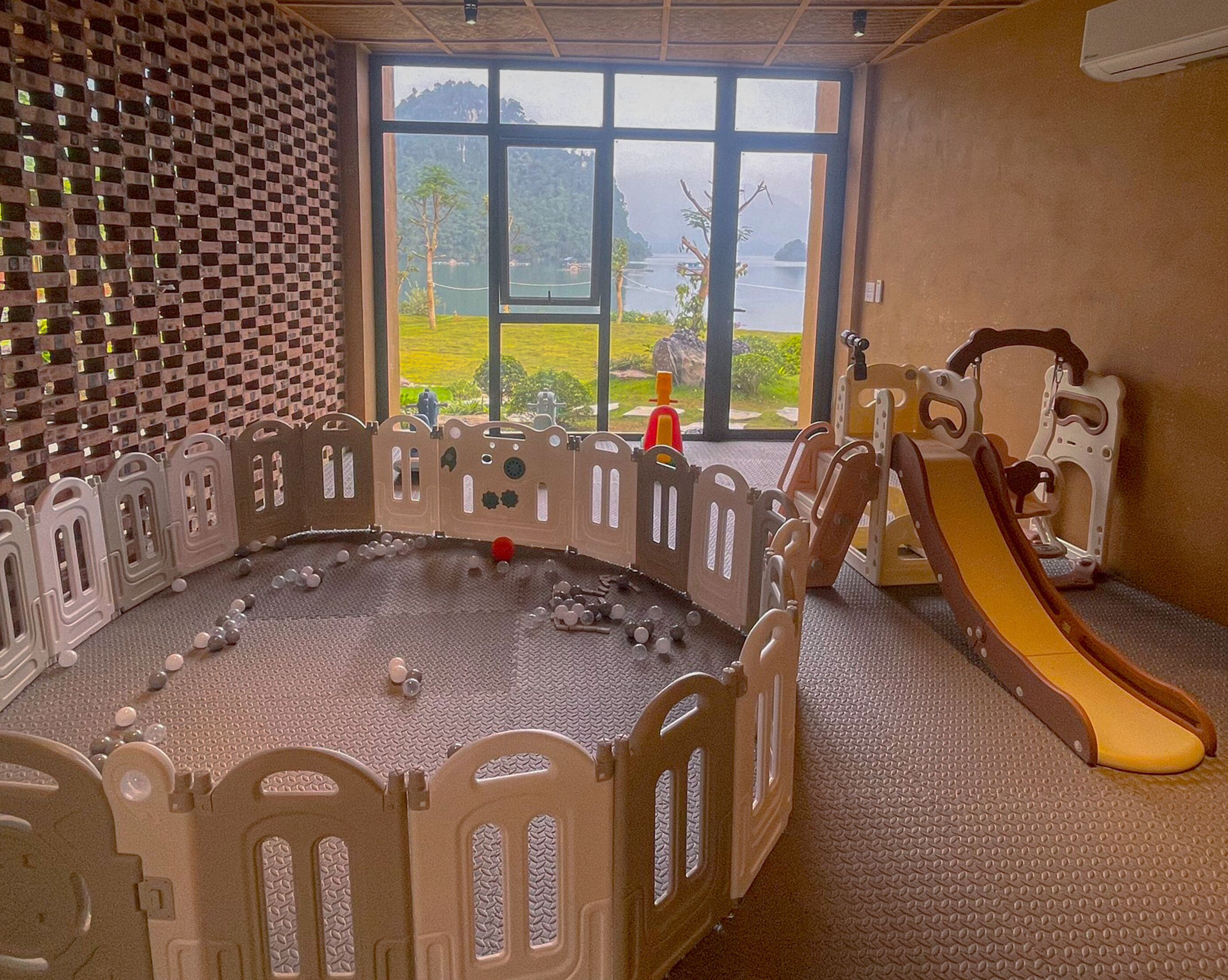 A play area with a slide, a climbing structure, and a view of a lake through large windows.