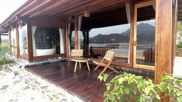 A wooden covered patio with a stone floor, large windows, and a view of a lake and mountains.