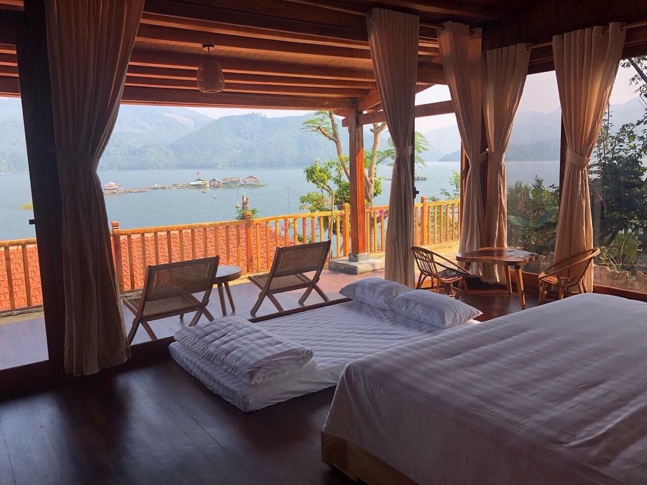 A room with a bed, two chairs, a small table, and a view of a lake and mountains.