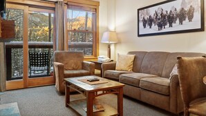 Una sala de estar acogedora con sofá, sillón y mesa de centro, una ventana con vistas y un cuadro en la pared.