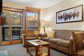 Una sala de estar acogedora con sofá, sillón y mesa de centro, una ventana con vistas y un cuadro en la pared.