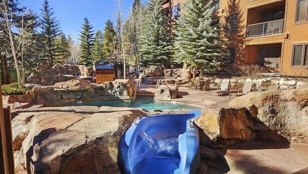 Un área de piscina con jacuzzi, sillas de descanso y un edificio con balcones.