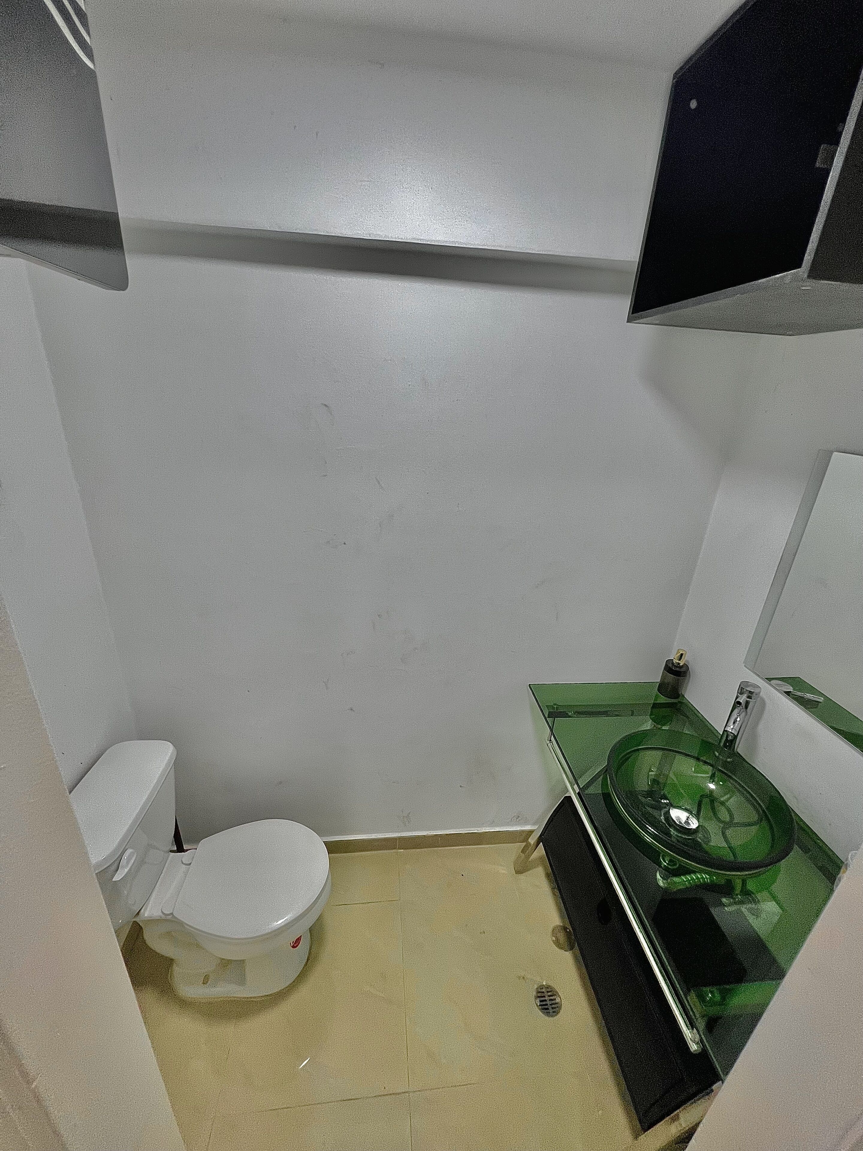 A small bathroom with a white toilet, a green glass sink, and a mirror above the sink.