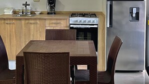 A modern kitchen with wooden cabinets, a stainless steel refrigerator, a built-in oven, and a dining area with wicker chairs. - Apartment in Caracas  (Caracas)